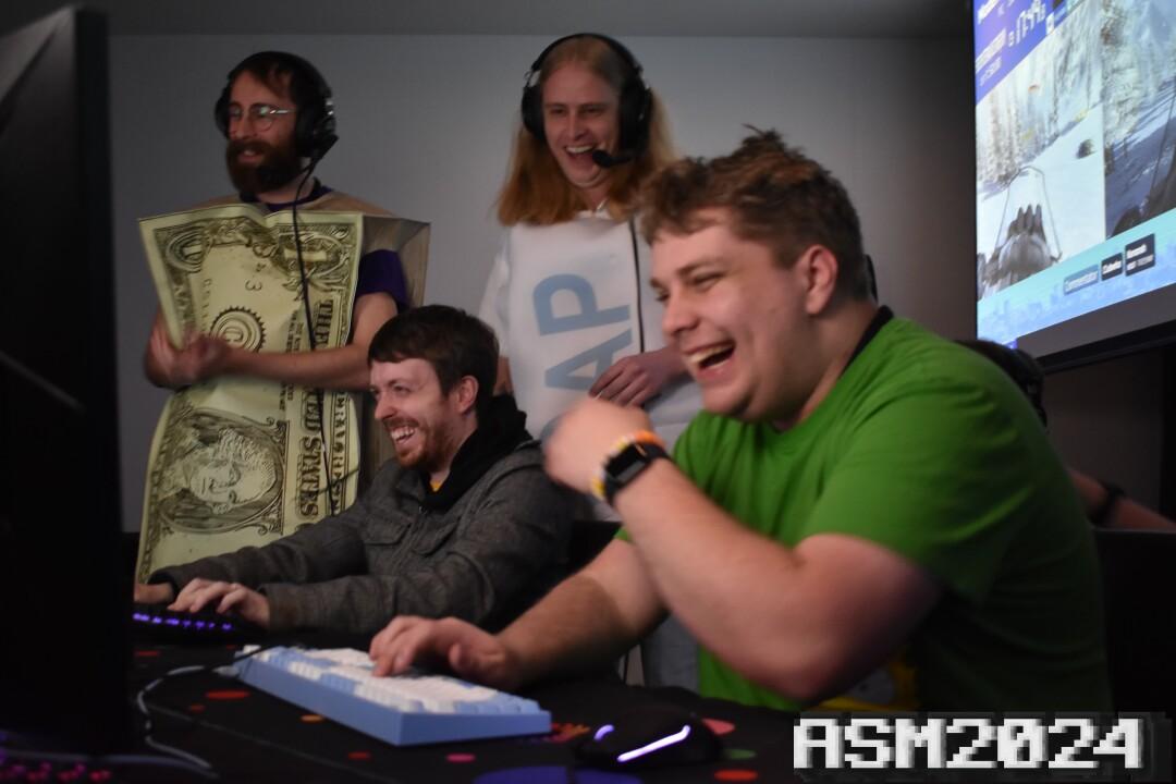 ZoomieG dressed as a bar of soap, Softman25 dressed as a stack of dollar bills and Astrious dressed as himself, laugh at LiquidWifi at ASM2024